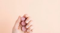 Woman's hand with manicured nails displaying soft pink nail polish against neutral beige background, suitable for beauty, cosmetics, and wellness marketing materials.