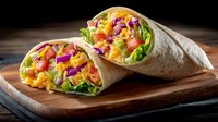 Fresh vegetable wrap with colorful lettuce, tomatoes, corn and purple cabbage on wooden cutting board for healthy meal preparation and dining.