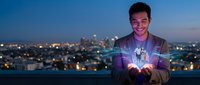Young Asian businessman holding glowing digital hologram with futuristic technology interface against city skyline at dusk for innovation concepts.