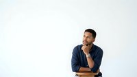 Young man with dark hair and medium skin tone wearing navy blue shirt, hand on chin in thoughtful pose against white background, suitable for business and lifestyle content.