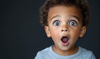Young African American child with curly hair and bright blue eyes expressing extreme surprise with mouth open wide and astonished facial expression against dark background.