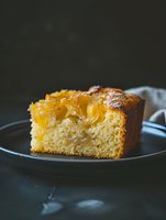 Caramelized pineapple upside-down cake slice on dark plate shows moist texture and golden fruit topping against moody background, perfect for food marketing.