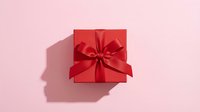 Red gift box with satin ribbon bow on pink background for holidays, celebrations, birthdays, anniversaries, Valentine's Day, Christmas presents and special occasions.