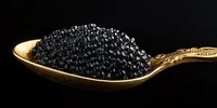 Black caviar on vintage golden spoon against dark background, luxury gourmet food close-up showing delicate texture and shine of sturgeon roe.