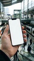 Hand holding smartphone with blank white screen in modern shopping mall with escalators and glass architecture for mobile app mockup presentations.