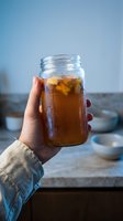 Hand holding glass jar filled with iced cola or cola beverage against blue sky background. Refreshing cold drink for summer beverage advertising and lifestyle content.