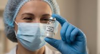 Female healthcare professional in mask and gloves holding a clinical trial sample vial in a medical laboratory setting.