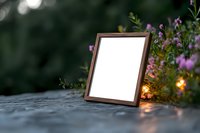 Empty wooden photo frame with white mockup display on stone surface surrounded by purple wildflowers and soft glowing lights in garden setting at dusk.