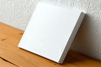 Blank white square canvas mockup leaning against wall on wooden surface, ready for artwork display. Clean minimal presentation for designers and artists.
