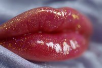 Sensual red lips with shimmering gold glitter makeup in macro shot against soft gray background, showing glossy finish and detailed texture for beauty and cosmetics.
