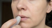 Woman applying white lip balm stick to lips for moisturizing skincare routine and lip care treatment.