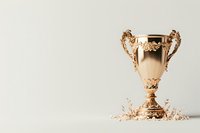 Elegant golden trophy cup with ornate handles and decorative base on light background, surrounded by metallic confetti pieces for achievement celebration.