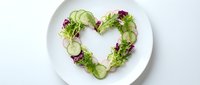 Fresh cucumber slices and purple cabbage arranged in heart shape on white plate for healthy eating, diet, nutrition, and wellness concepts.
