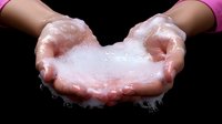 Cupped hands holding white soap foam and bubbles against black background, close-up view showing personal hygiene and cleanliness concept.