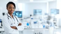 Confident African American female doctor with stethoscope standing with crossed arms in modern hospital setting. Professional healthcare worker portrait.