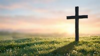 Wooden cross silhouette on grassy hill at sunrise with soft pastel sky and golden sunlight creating peaceful spiritual atmosphere for worship and faith.