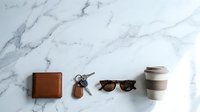 Brown leather wallet with keys and sunglasses arranged on white marble surface. Minimalist flat lay composition for lifestyle and fashion concepts.