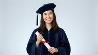 Happy young Asian woman graduate in cap and gown holding diploma certificate smiling at camera on white background isolated for education design.