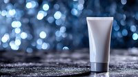 White cosmetic tube on glitter surface against blurred blue bokeh lights background, luxury skincare product photography for beauty and spa marketing.