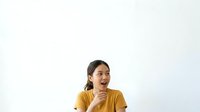 Young woman with dark hair and East Asian ethnicity wearing mustard yellow t-shirt, hand on chin in thoughtful pose against white background, isolated for design use.