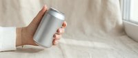 Female hand holding blank aluminum beverage can mockup on neutral beige background. Clean minimalist product presentation for branding and packaging design.