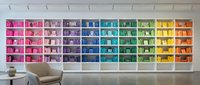 Modern rainbow bookshelf wall with color-coded books arranged in spectrum from pink to orange, contemporary interior design for home library organization.