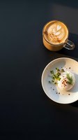 Cappuccino with latte art and gourmet plated appetizer featuring creamy cheese, microgreens, and red pepper on dark surface for restaurant, cafe, and food styling use.