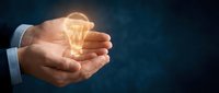 Businessman holding glowing lightbulb in cupped hands against dark blue background, symbolizing innovation, creativity, and new business ideas for entrepreneurship concepts.