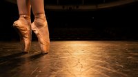 Ballerina feet in pointe shoes on wooden stage floor. Professional dancer performing classical ballet with elegant technique and grace.
