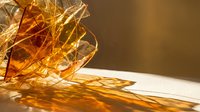 Golden amber resin or glass fragments scattered on white surface with warm sunlight casting translucent shadows, suitable for abstract backgrounds and design projects.