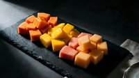 Colorful cheese cubes arranged on dark slate board featuring orange cheddar, yellow gouda and pink varieties for gourmet appetizer presentation.