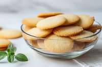 Homemade butter cookies in glass bowl with fresh mint leaves on white background, selective focus on golden crispy biscuits, food photography.
