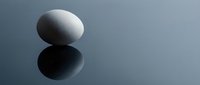White egg on reflective surface with mirror reflection creating minimalist composition for wellness and nutrition concepts.