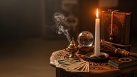 Mystical fortune telling scene with tarot cards, crystal ball, burning candle and ancient books on wooden table creating atmospheric divination setting.