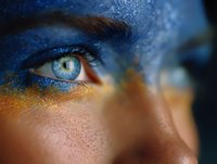 Close-up view of bright blue eye with artistic face paint in vibrant blue and gold colors creating ethereal makeup look for creative beauty and fashion photography.