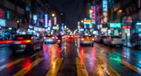 Blurred night city street with colorful neon lights reflecting on wet pavement, cars and traffic creating bokeh effect for urban backgrounds.