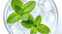 Fresh mint leaves floating in sparkling water with ice cubes in glass, refreshing summer drink concept for beverage and cocktail designs.
