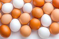 Fresh brown and white chicken eggs arranged in rows on light background, creating natural pattern for food industry and healthy eating concept.
