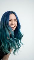 Young woman with vibrant blue and teal ombre hair laughing joyfully against white background. Creative hair coloring and styling concept.
