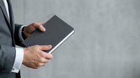 Businessman holding black notebook against gray background, professional business concept for corporate communication and planning.