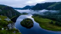 Dramatic aerial view of a curved river with small forested island surrounded by steep cliffs and morning fog in mountainous landscape, reflecting moody atmosphere.