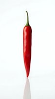 Red chili pepper isolated on white background with green stem, ready for culinary, food packaging, and recipe design projects.