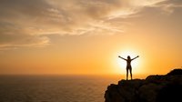 Silhouette of person with raised arms celebrating success on cliff edge during golden sunset over ocean horizon creating inspirational freedom moment.