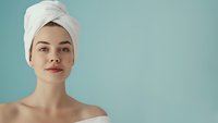 Young Caucasian woman wearing white towel on head and shoulders against turquoise background, fresh glowing skin, natural makeup look for spa and beauty concept.