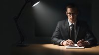 Professional businessman in suit working late at office desk under dramatic lamp lighting for corporate and business concepts.