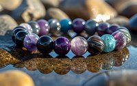 Colorful gemstone bracelet with amethyst, turquoise, and agate beads on reflective surface, showcasing natural stone jewelry with purple and blue tones in macro photography.