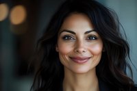 Young woman with long black wavy hair and warm smile, appearing confident and approachable. Suitable for business, lifestyle, wellness, and professional portrait use.