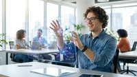 Young Hispanic businessman with curly hair and glasses gesturing while presenting in modern office with colleagues working in background.