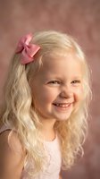 Young blonde girl with pink bow smiling joyfully in portrait studio session with warm background for children photography and family memories.
