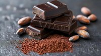 Dark chocolate pieces stacked with cocoa powder and raw cacao beans on dark background, macro food photography showing texture and layers of gourmet dessert.